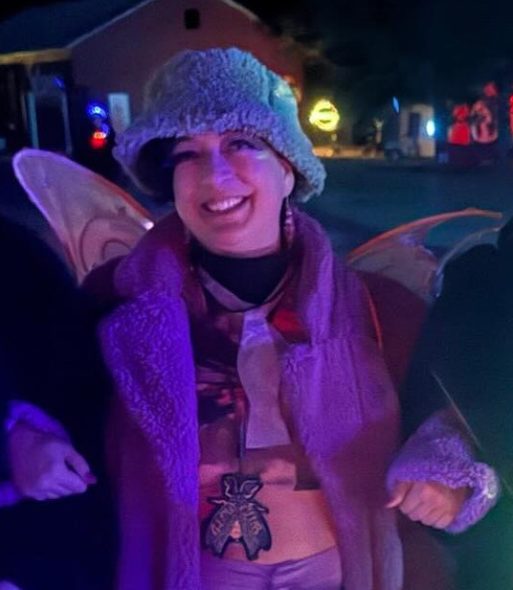 Beth at night, wearing a fuzzy green bucket hat, fuzzy purple coat, and fairy wings
